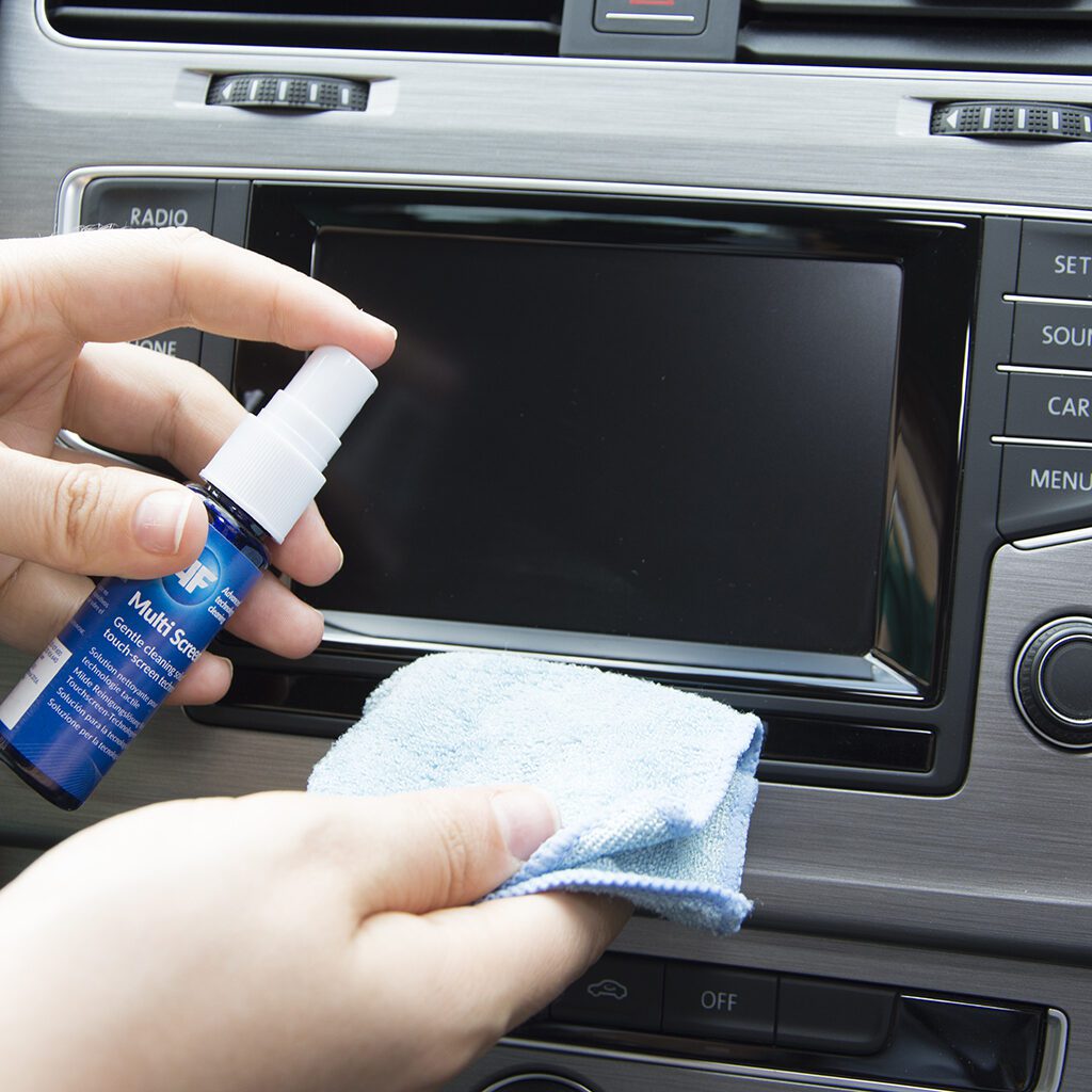 Cleaning car touchscreen with spray and cloth.
