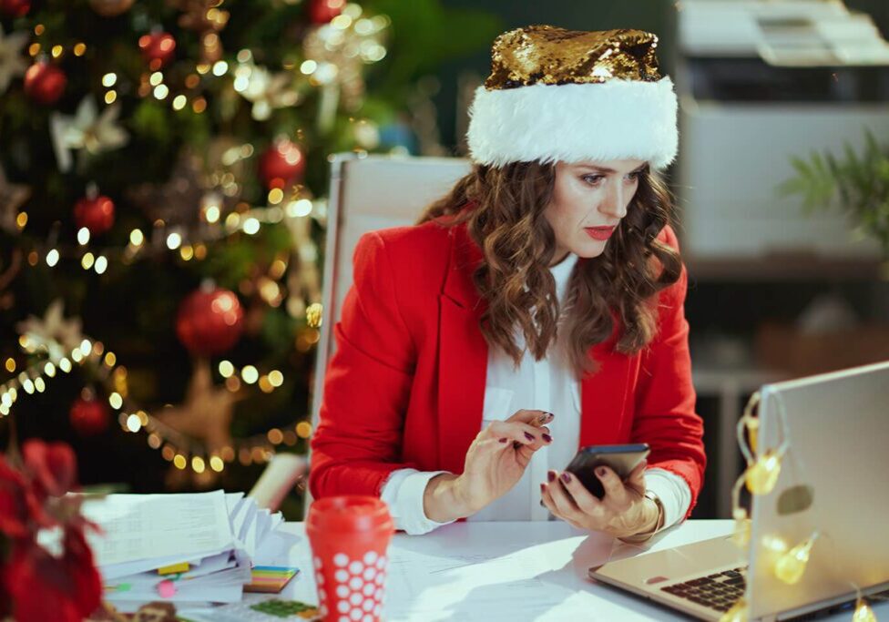 Woman in Santa hat using phone at desk.